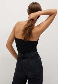 Top noir sans bretelles avec texture côtelée, associé à un jean noir taille haute avec deux poches arrière. Les cheveux du mannequin sont attachés en queue de cheval.