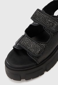 Sandali neri con tomaia sintetica texturizzata, dotati di due cinturini regolabili, design open toe e suola in gomma nera spessa.