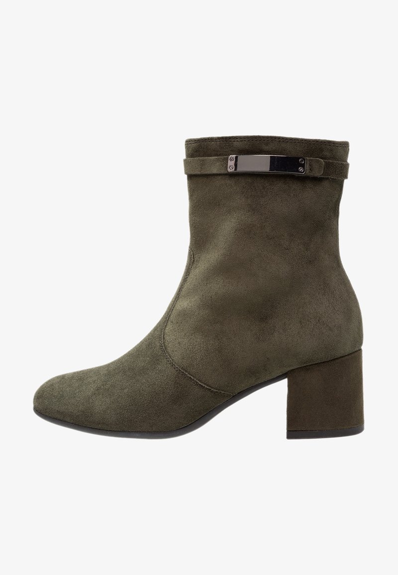 Botín de tobillo en ante verde oliva con punta cuadrada y un tacón grueso. Presenta una tira delgada con herrajes metálicos en el puño.