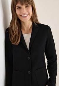 Blazer nero con due tasche frontali, design a un petto e due bottoni. Tessuto liscio con vestibilità slim e colletto a punte.