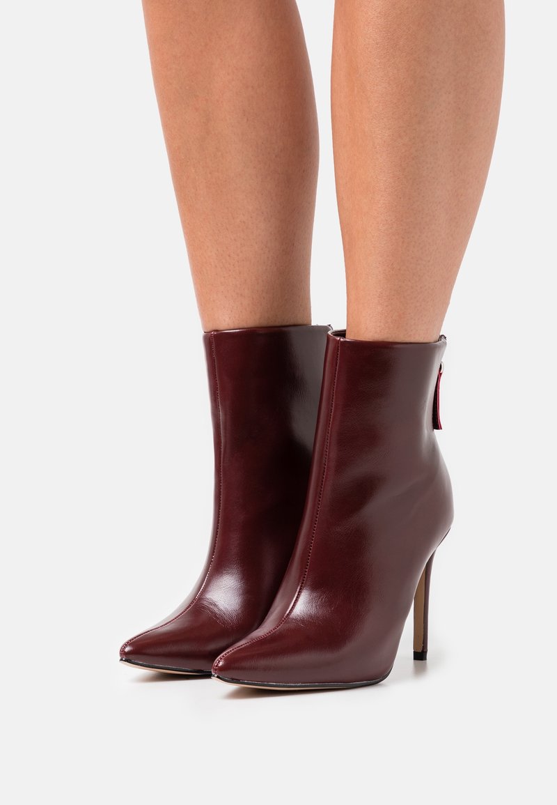 Bottes basses en cuir bordeaux avec un bout pointu, un talon stiletto haut et un détail de fermeture éclair à l'arrière. Texture lisse et design élégant.