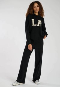 Svart hoodie med "LA"-grafik i krämfärg, matchad med svarta vida byxor. Mjuk tygkvalitet och avslappnad passform, med huva och långa ärmar.