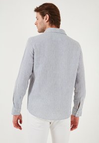 Cămașă cu mânecă lungă și dungi în albastru deschis și alb din bumbac, având guler, manșete cu nasturi și o croială relaxată cu slituri laterale.