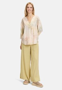 Camicia leggera a fantasia pastello con scollatura a V e maniche lunghe, abbinata a pantaloni larghi in lino giallo pallido e espadrillas in tonalità neutra.