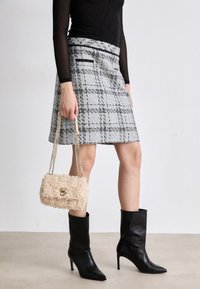 Γκρι και μαύρη καρό φούστα με ίσια γραμμή, συνδυασμένη με μαύρες μυτερές μπότες μέχρι τον αστράγαλο και μια μπεζ χνουδωτή τσάντα χειρός με χρυσό κούμπωμα.