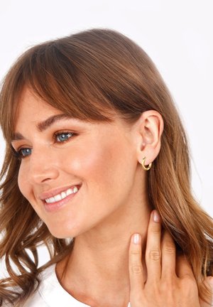 Goldene Creolen mit einem glatten, runden Design. Das Model hat lange, wellige braune Haare und ein Oberteil in neutralen Farben.