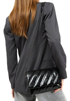 Sort quiltet crossbody taske med skinnende, tekstureret materiale, der har en kæderem og rektangulær form. Båret sammen med en mørk blazer.