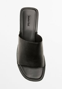 Zwarte leren slipper met een brede, overlappende band, vierkante neus en een textuur op de voetbed. Minimalistische constructie met een gladde afwerking.