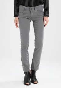 Jeans gris ajustados de algodón. Cuenta con bolsillos frontales, cierre de botón y costuras sutiles. Combinados con sandalias de tacón negras.