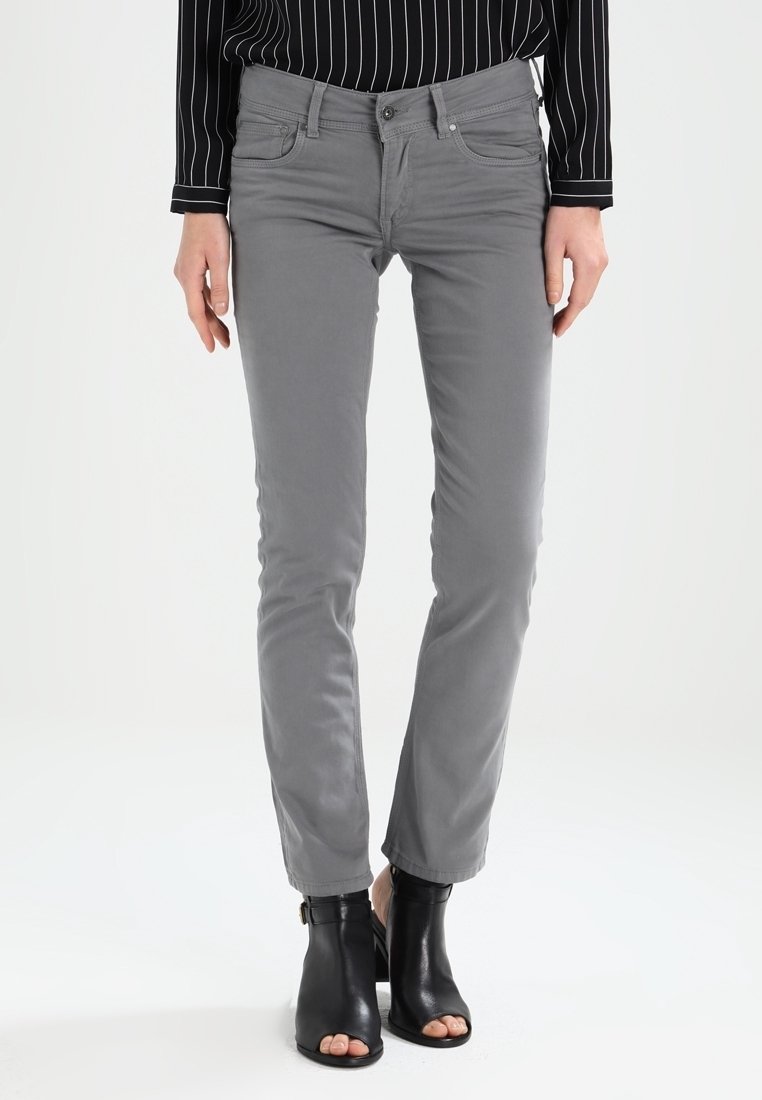 Jeans gris ajustados de algodón. Cuenta con bolsillos frontales, cierre de botón y costuras sutiles. Combinados con sandalias de tacón negras.