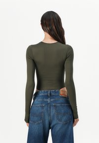 Olive green long-sleeve bodysuit with smooth texture, paired with high-waisted blue denim jeans featuring a label on the back.