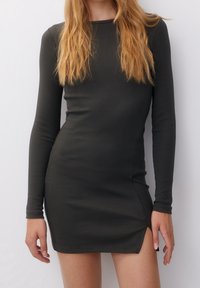 Robe mini à manches longues et côtelées en gris foncé, avec un col rond et des fentes latérales pour plus de mobilité. Texture lisse avec une silhouette ajustée.