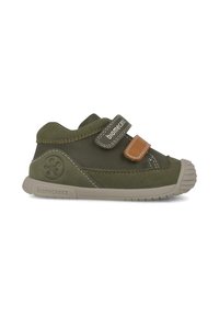 Chaussure en daim vert avec accent en cuir beige, bande Velcro, semelle en caoutchouc et bout renforcé. Présente des détails de couture et un logo sur le côté.