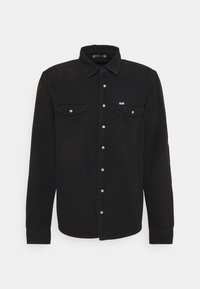 Camisa de mezclilla negra de manga larga, con cuello puntiagudo, dos bolsillos en el pecho, cierre con botones plateados y detalles de costura sutil.
