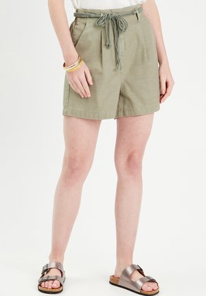 Pantalones cortos caqui con cinturilla ajustable, frente con pliegues y bolsillos laterales. Combinados con sandalias metálicas y múltiples pulseras.
