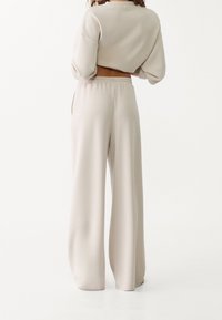 Beige cropped sweatshirt med rund halsudskæring og løs pasform, parret med vide bukser med snor i livet i matchende materiale og farve.