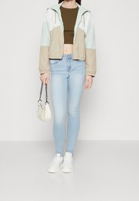 Kurtka w kolorze beżowym, miętowym i białym, z krótkim krojem. Połączona z jasnoniebieskimi wąskimi dżinsami i białymi butami. Trzymając białą torebkę.