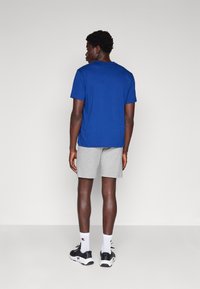 Camiseta azul y pantalones cortos grises. La camiseta tiene un escote redondo sencillo; los pantalones cortos son de longitud hasta la rodilla. Se lleva con zapatillas negras y calcetines blancos.