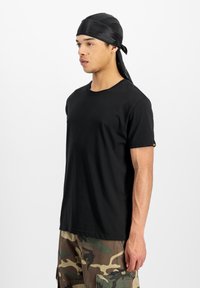 T-shirt noir à manches courtes en coton, avec un col rond et un petit logo sur la manche gauche, associé à un pantalon cargo camouflage.
