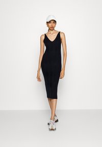 Robe midi noire en tricot avec un décolleté en V et une texture côtelée, offrant une coupe ajustée. Assortie à une casquette blanche et des baskets.
