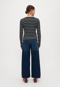 Black and white striped long-sleeve top paired with wide-leg dark blue jeans and red shoes. Smooth fabric with fitted silhouette.