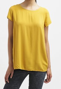 Blouse jaune à manches courtes avec un col rond, fabriquée en tissu doux. Le haut a une coupe décontractée et un ourlet légèrement arrondi.