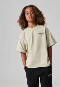Heled roheline oversized T-särk lühikeste varrukatega, ümmargune kaelus ja must "ALLSAINTS" logo. Koos mustade pükstega, millel on valge logo.
