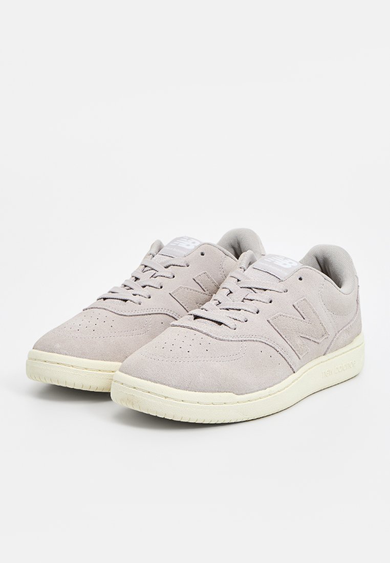 Zapatillas de ante gris claro con caja de dedos perforada, cordones planos, un collar acolchado y suela de goma. Presentan un logo en relieve en el lateral.