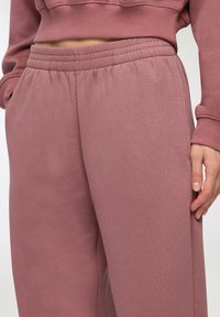 Set di felpa e pantaloni jogger rosa realizzato in tessuto morbido. I pantaloni jogger presentano una vita elasticizzata e tasche laterali, con un design a vestibilità comoda.