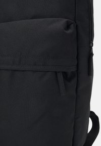 Black fabric backpack with a zippered pocket and a textured surface. Features include a side handle and a smooth strap for carrying.