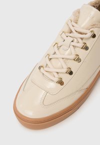 Baskets en cuir verni crème avec un bout arrondi, doublure textile beige, œillets dorés et lacets plats beiges. Semelle en caoutchouc avec surface texturée.