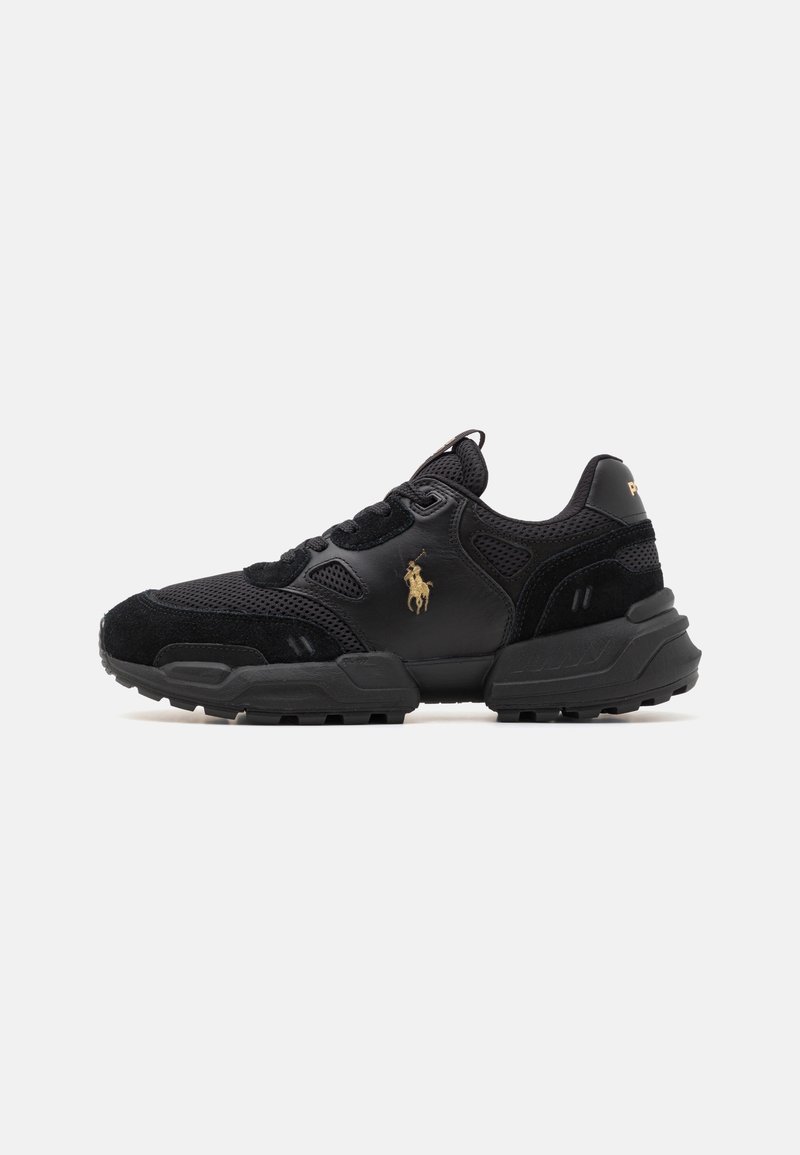 Schwarze Sportschuhe aus einer Kombination von Wildleder und Mesh-Materialien, mit runder Form, strukturiertem Außensohle und einem goldenen Emblem auf der Seite.