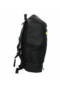 Mochila negra con un exterior suave y un bolsillo lateral de malla, con tiradores de cremallera de un brillante color verde. Correas resistentes y un asa en la parte superior para llevarla.