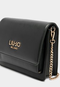 Borsa a tracolla in pelle nera con logo in tonalità oro, chiusura a patta e tracolla a catena. Texture liscia con minimi dettagli e forma strutturata.