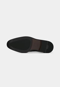 Semelle noire d'une chaussure avec un design pointu. Présente une finition lisse avec une zone texturée près du centre. Matériau en caoutchouc durable.