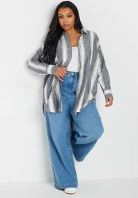 Camisa de botón a rayas gris y blanca con mangas largas, combinada con jeans de pierna ancha de cintura alta en azul claro y zapatillas blancas.