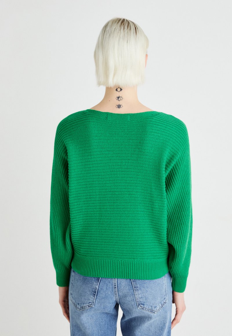 Grüner gestrickter Pullover mit rundem Halsauschnitt, langen Ärmeln und geripptem Saum. Verfügt über ein strukturiertes Muster und einen lockeren Schnitt, kombiniert mit hellblauen Jeans.