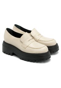 Beżowe skórzane mokasyny z zaokrąglonym czubkiem, z detali paska z przodu oraz grubą czarną gumową podeszwą o teksturowanym wykończeniu.