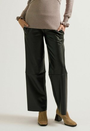 Pantalon large en simili cuir noir avec plis à l'avant, associé à un pull beige côtelé avec des poignets à volants et des accents de boutons.