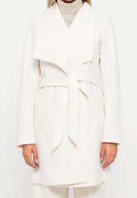 Vit ullblandad kappa med bred krage, självbindande bälte och sidofickor. Rak passform och långa ärmar, som presenterar en ren, minimalistisk design.