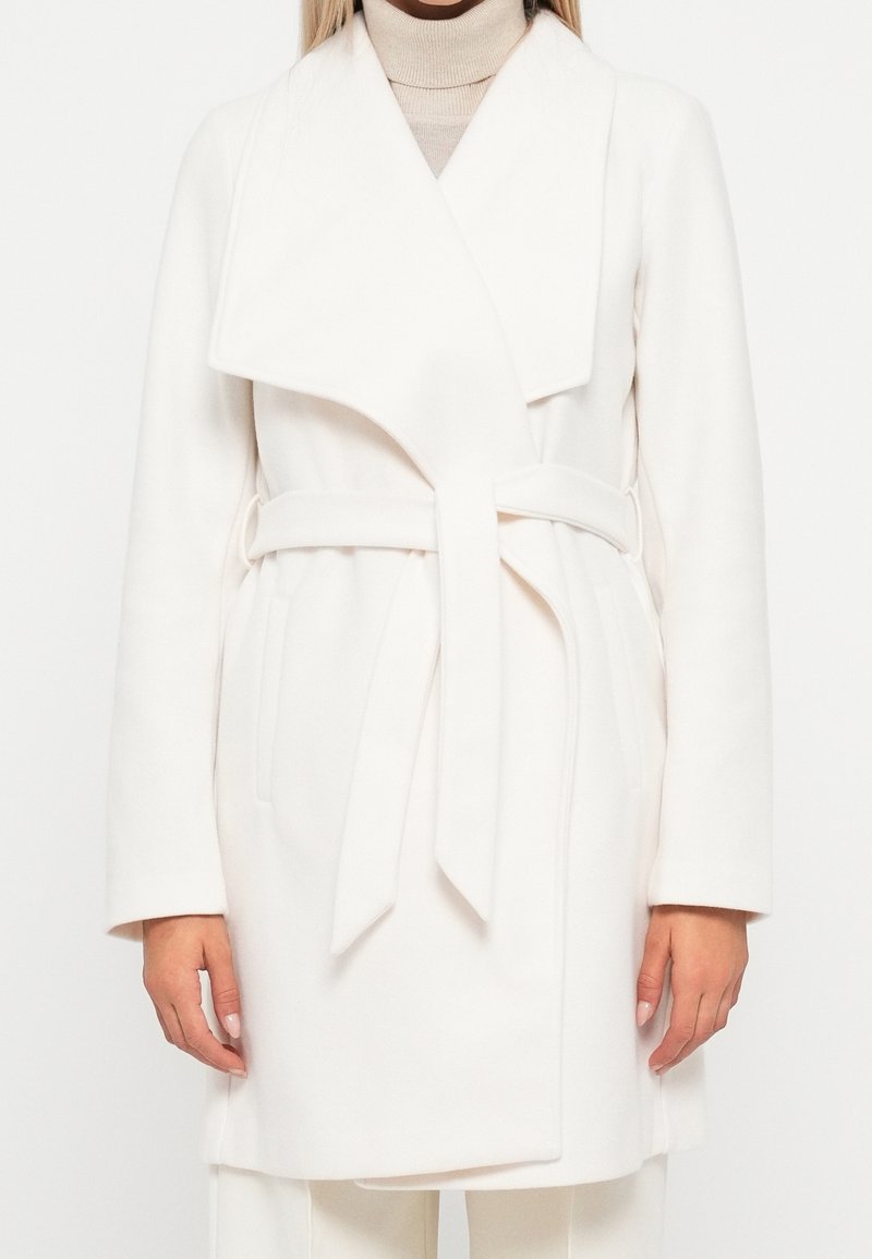 Vit ullblandad kappa med bred krage, självbindande bälte och sidofickor. Rak passform och långa ärmar, som presenterar en ren, minimalistisk design.