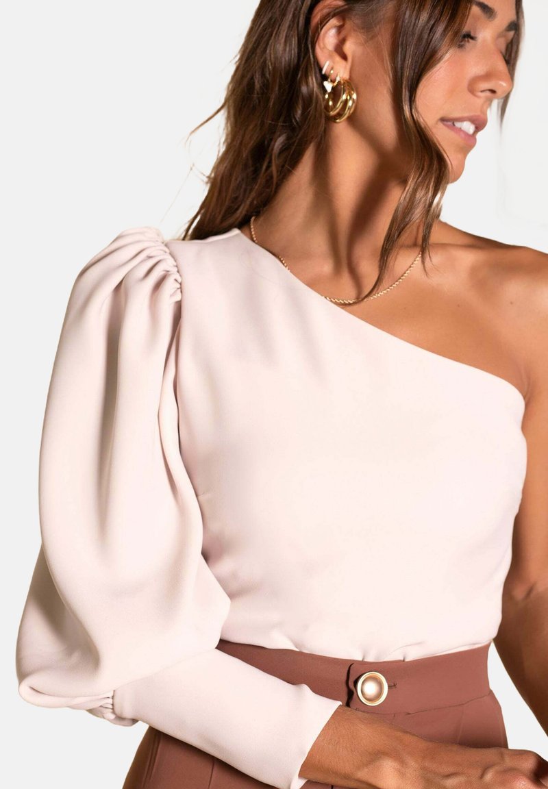 Blusa de un solo hombro en suave tela rosa con una manga abullonada. Presenta un corsé ajustado y un cinturón de tiro alto en marrón contrastante con un botón.