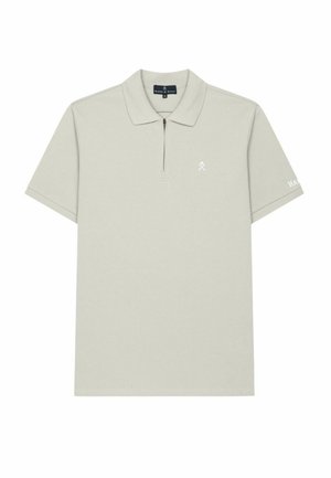 Polo de manga corta color beige claro con cuello con cremallera, un pequeño logo blanco en el pecho y marca en la manga izquierda.