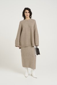 Beige gestricktes Sweatshirt und Midirock-Set mit Rippstruktur. Kombiniert mit weißen spitzen Stiefeln und einer kleinen schwarzen Handtasche.