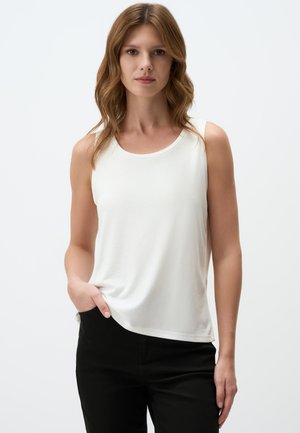 Top sans manches blanc en tissu doux avec un col rond, associé à un pantalon noir, présente une coupe décontractée et un drapé subtil.