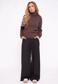 Brązowy, dopasowany sweter z golfem o teksturowanym splocie; szerokie, czarne spodnie z wysokim stanem; białe trampki z beżowymi akcentami.