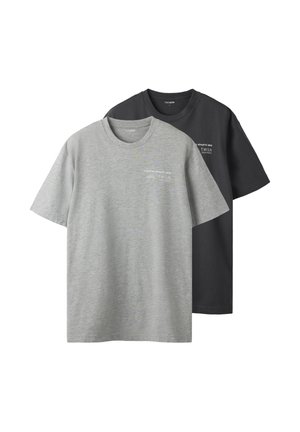 Δύο απλά T-shirts με στρογγυλή λαιμόκοψη, ένα γκρι και ένα μαύρο, το καθένα με μικρό λευκό κείμενο στο πάνω αριστερό μέρος του στήθους.