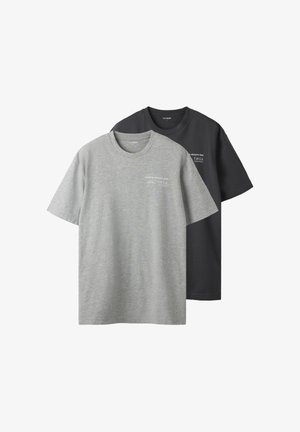 To ensfarvede crewneck-T-shirts, en grå og en sort, hver med en lille hvid tekst øverst til venstre på brystet.