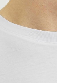 Witte t-shirt stof die een close-up van de halslijn laat zien met ribbeldetail, een gladde textuur en gelijkmatige stiksels, die de eenvoud van het ontwerp benadrukt.