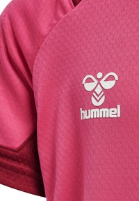 Pink sportsjersey lavet af tekstureret stof, med et hvidt Hummel-logo og en kontrasterende maroon accent på ærmet.
